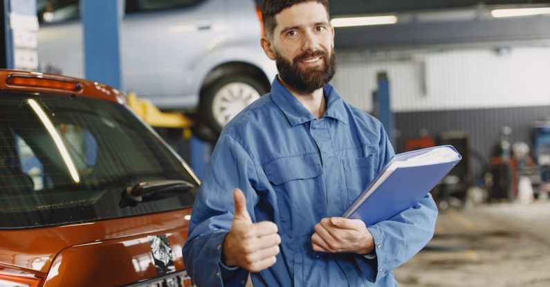 Car Brakes - Man in Blue Coveralls Standing in an Auto Repair Shop Doing an Ok Hand Gesture