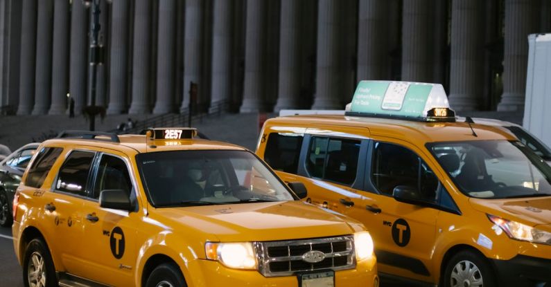 Minivans Vs. SUVs - Stylish modern yellow SUV and minivan taxi cars with glowing headlights on city street near aged building with columns at sunset